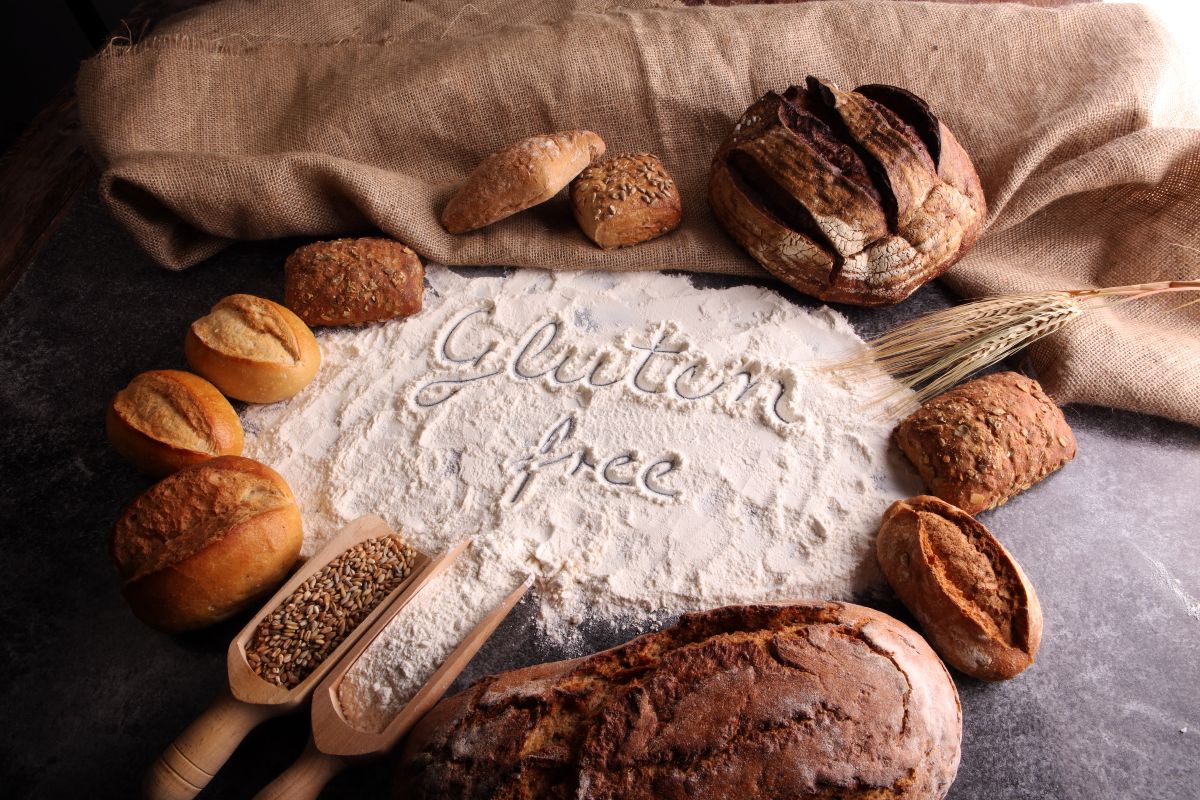 Senza glutine: come convivere con la celiachia 2 Della farina sparsa su un tavolo con la scritta gluten free e delle pagnotte di pane
