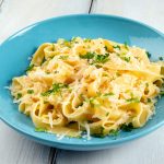 Pasta burro e parmigiano: un primo piatto sano e veloce 1 su tavolo di legno bianco, piatto azzurro con pasta burro e parmigiano con una spolverata di prezzemolo