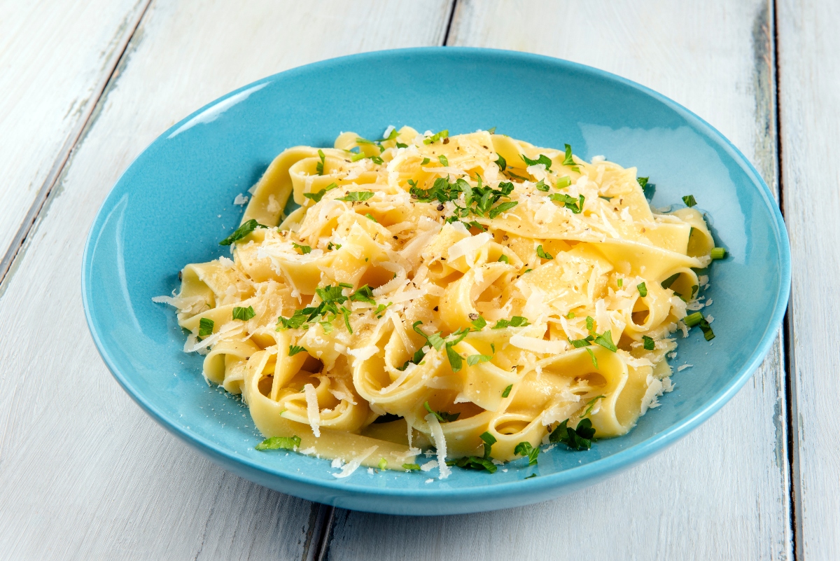Sughi per pasta fatti in casa: ricette veloci e sane piene di gusto 6 su tavolo di legno bianco, piatto azzurro con pasta burro e parmigiano con una spolverata di prezzemolo