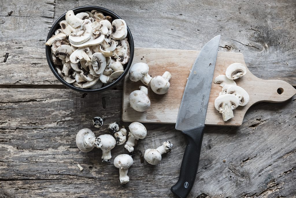 Risotto ai funghi: primo piatto cremoso e gustoso, pronto in pochi passaggi 2 in primo piano su un tagliere di legno dei funghi champignon e un coltello