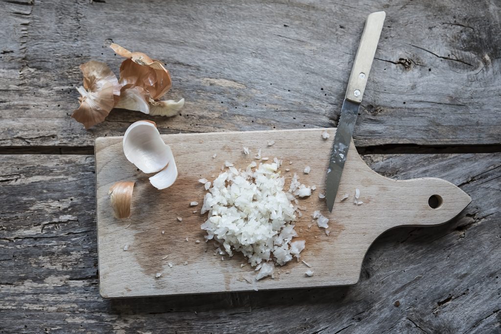 Risotto ai funghi: primo piatto cremoso e gustoso, pronto in pochi passaggi 3 in primo piano un tagliere di legno con della cipolla tritata finemente
