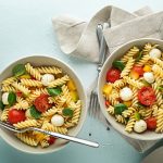 Pasta pomodori e mozzarella: un delizioso primo piatto freddo, estivo e colorato 1 su sfondo verde chiaro 2 ciotole grandi con pasta pomodori e mozzarella e basilico