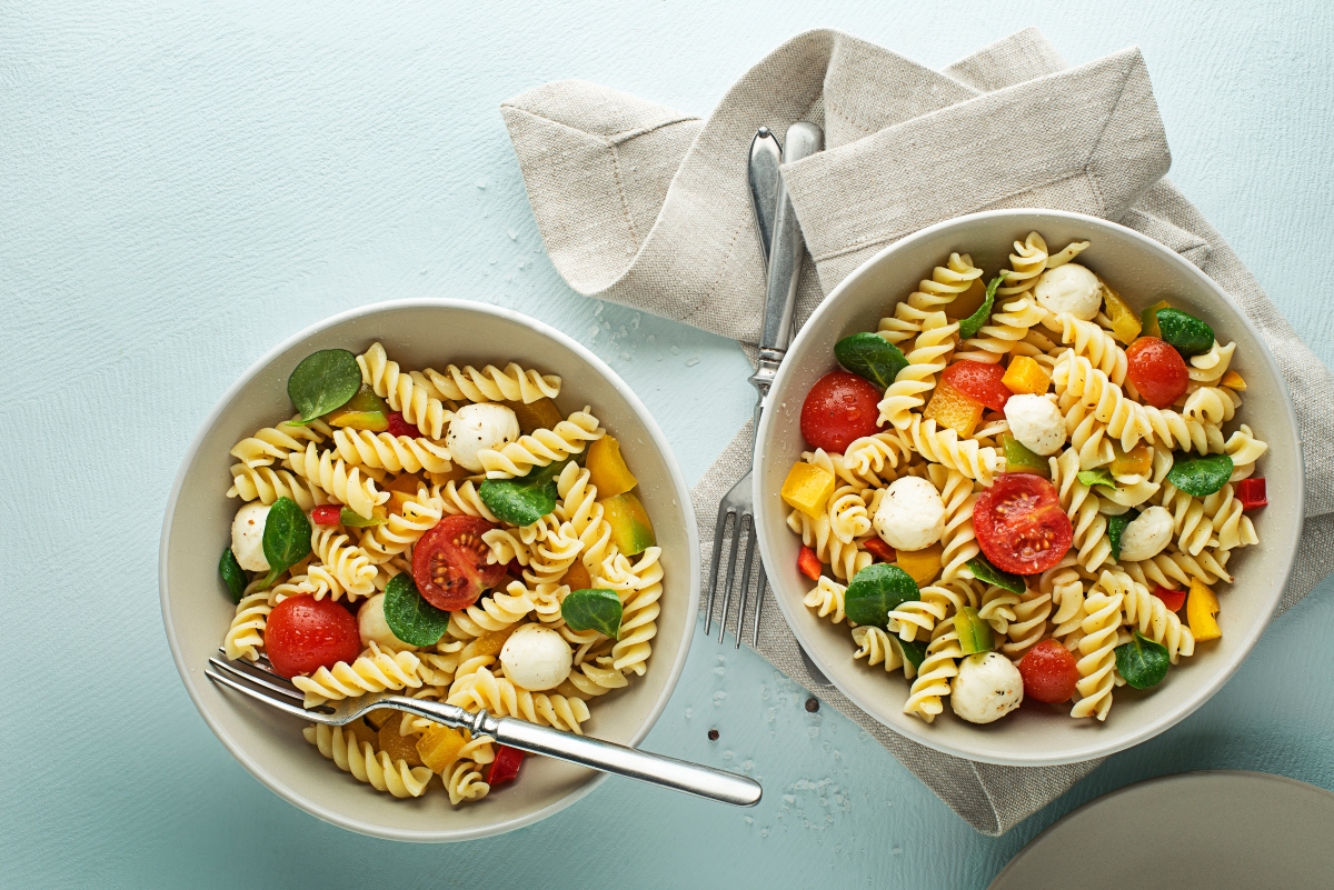 su sfondo verde chiaro 2 ciotole grandi con pasta pomodori e mozzarella e basilico