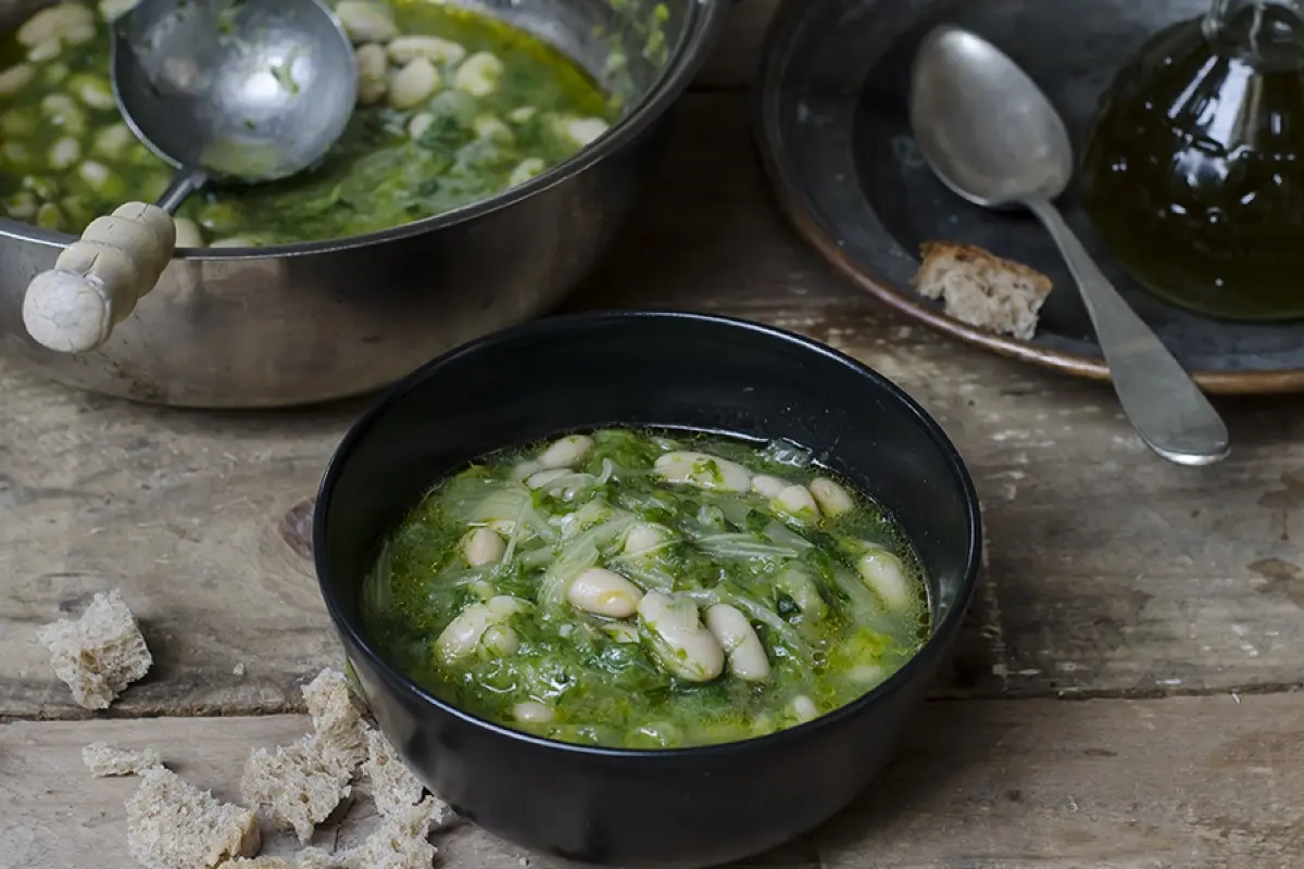 Minestre e zuppe: ricette da gustare quando fa freddo e non solo 13 Su tavolo di legno, pentola con zuppa di scarola e fagioli con un mestolo. Accanto piatto di zuppa pronta con cucchiaio