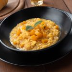 Risotto alla zucca cremoso: ricetta semplice anche con il Bimby 2 su piatto piano nero, scodella nera con dentro il risotto alla zucca