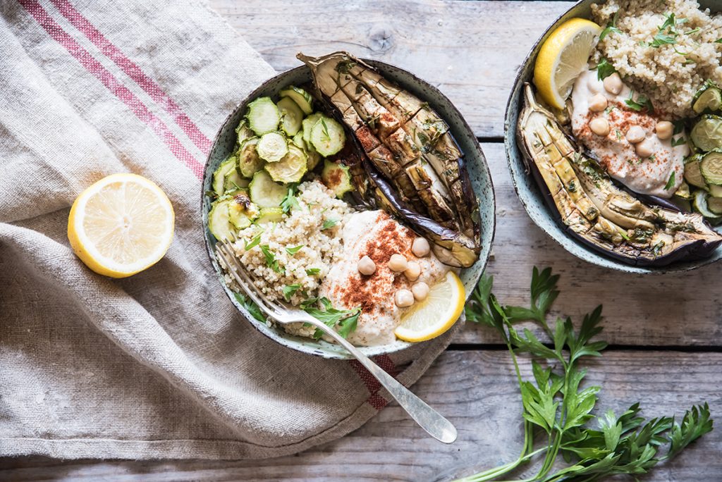 Buddha bowl con quinoa: la ricetta veloce per un piatto unico sano e gustoso 7 Su un tavolo di legno, un piatto di Buddha bowl con quinoa, zucchine e melanzane e accanto mezzo limone