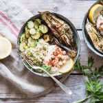 Buddha bowl con quinoa: la ricetta veloce per un piatto unico sano e gustoso 1 Su un tavolo di legno, un piatto di Buddha bowl con quinoa, zucchine e melanzane e accanto mezzo limone