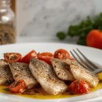 Filetti di pesce persico al forno: un secondo piatto leggero e veloce 1 In primo piano su un piatto bianco dei filetti di pesce persico al forno con pomodorini. Sullo sfondo dei pomodori e del prezzemolo.