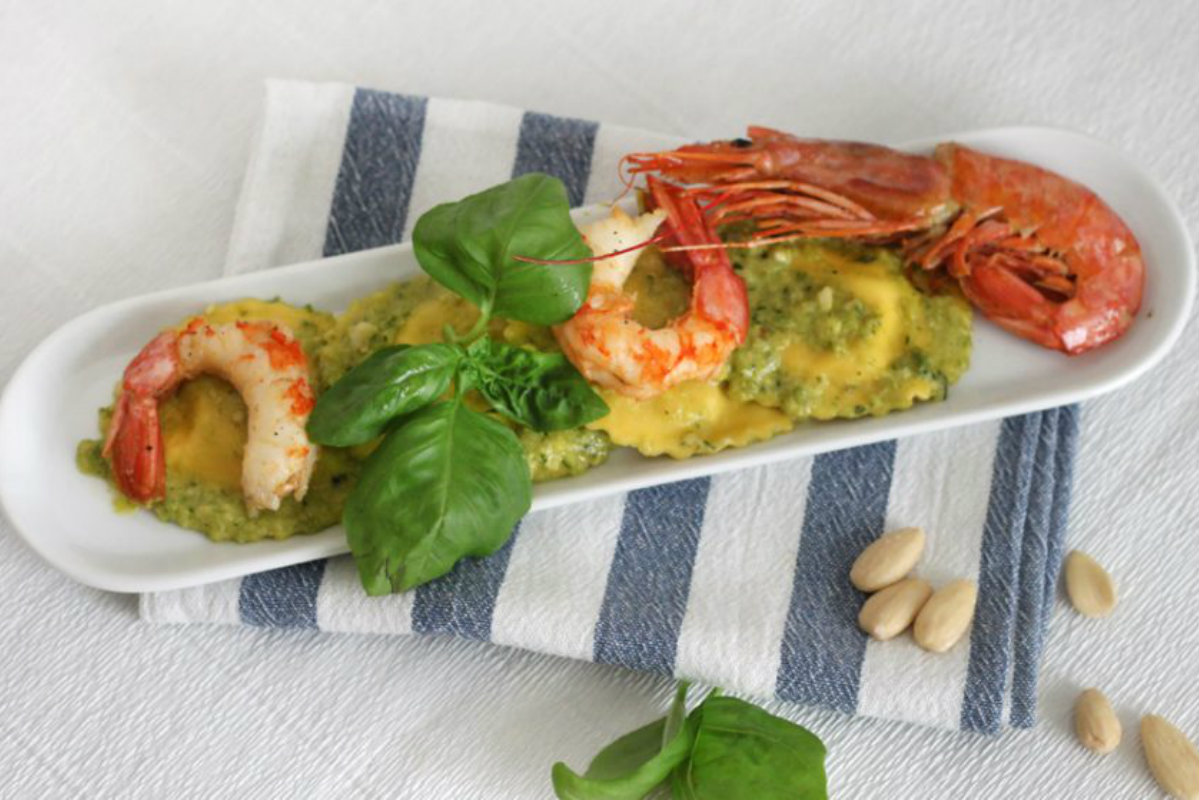 Ravioli: tante ricette semplici, gustose e innovative 2 piatto bianco allungato su tovagliolo con ravioli e gamberi, pinoli e foglie di basilico accanto