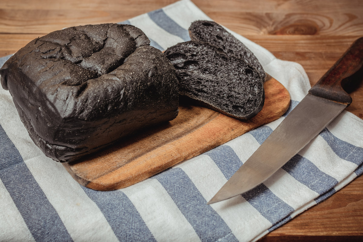 Carbone vegetale o attivo: a cosa serve, quando prenderlo e controindicazioni 3 un filoncino di pane al carbone vegetale su un tagliere