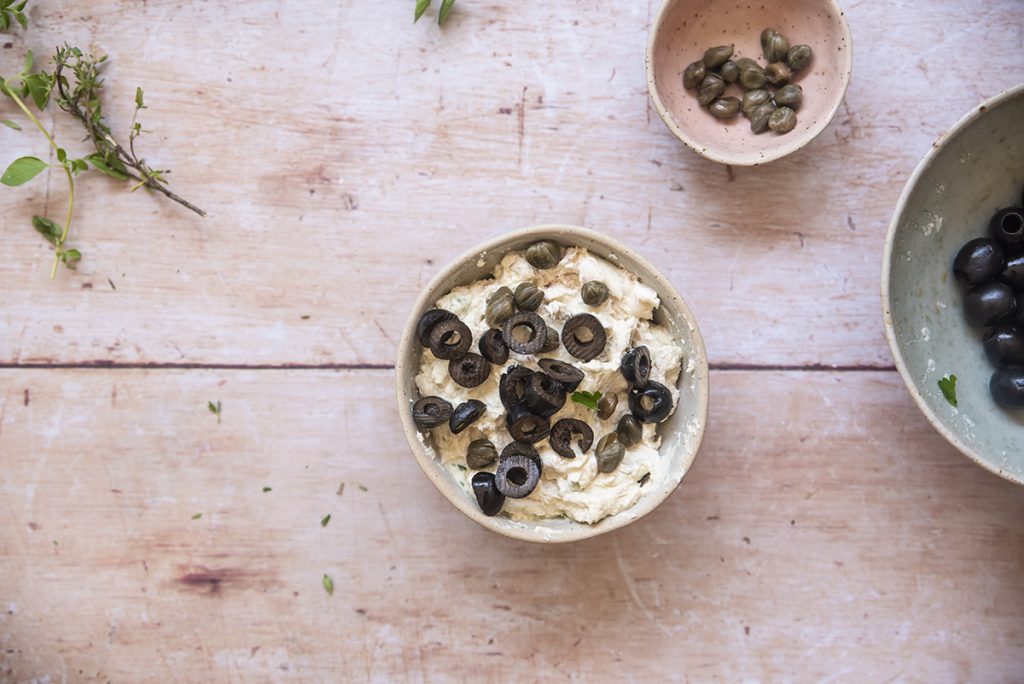 Panino con mousse di tonno, robiola, capperi e olive 2 due ciotole con mousse di tonno capperi e olive su una base di legno