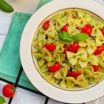 La pasta alla crudaiola: la ricetta sana, veloce e facile da preparare 1 su tavolo da cucina piatto bianco con pasta alla crudaiola con pomodori e basilico, sotto tovagliolo verde e attorno pomodorini e foglie di basilico