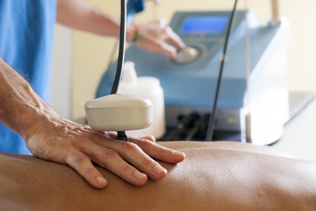 Tecarterapia: cos'è, benefici, prezzo e controindicazioni 1 tecarterapia: una mano che regge l'apparecchio per la tecarterapia su una schiena