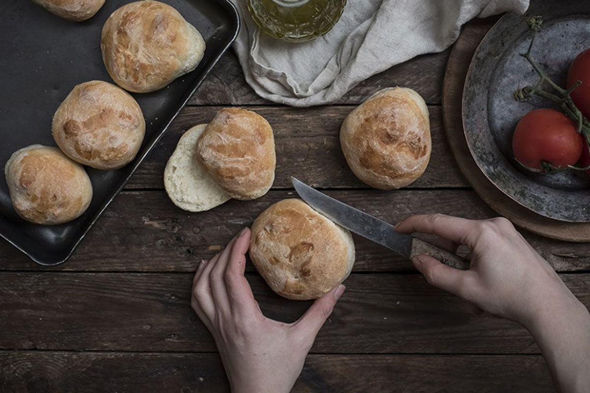 Pane fatto in casa: ricette genuine e semplici da provare 36 panini in una teglia e due mani che ne tagliano uno a metà