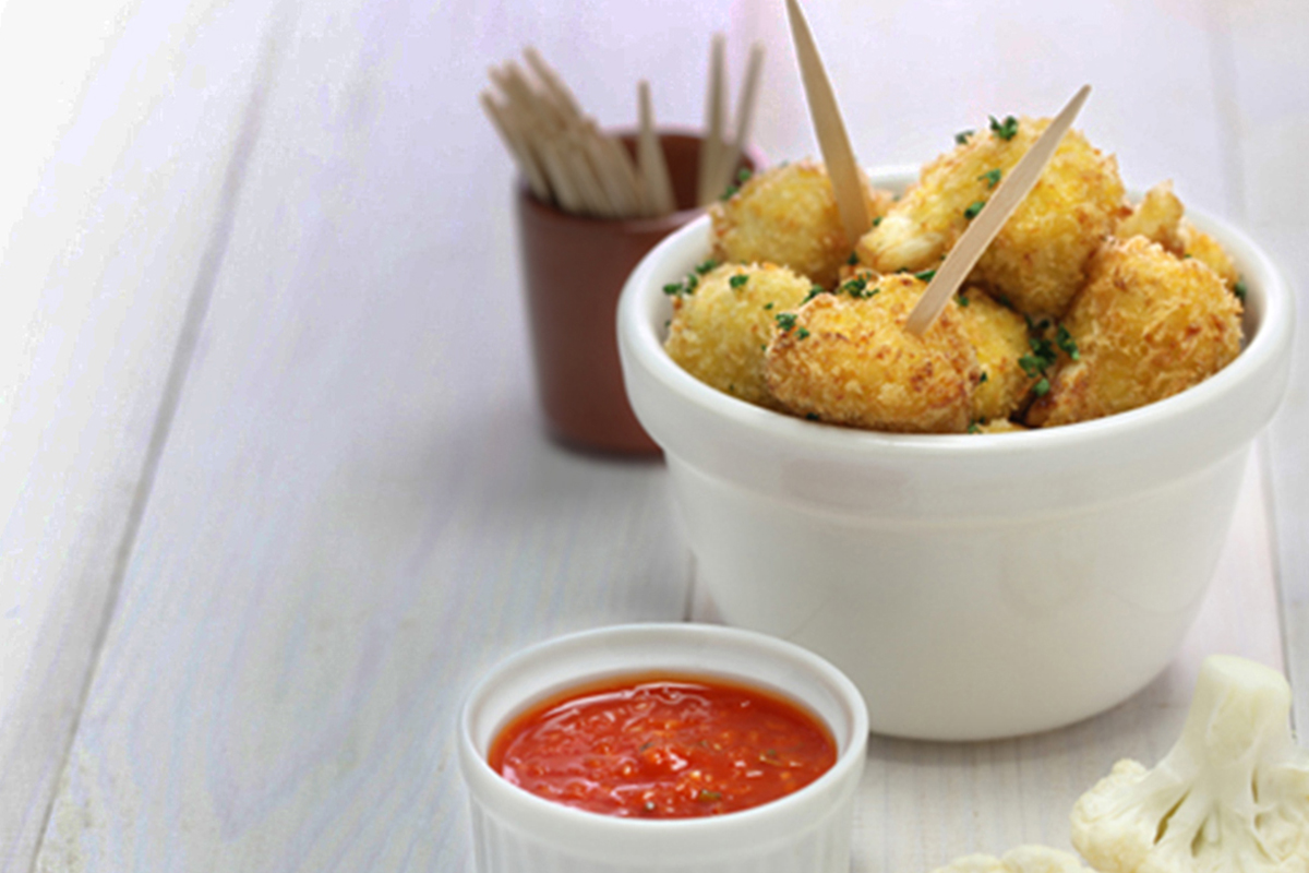 Ricette con miglio: 7 idee sane e nutrienti 5 Una ciotola con delle polpette di miglio e cavolfiore con accanto una ciotolina con salsa di pomodoro