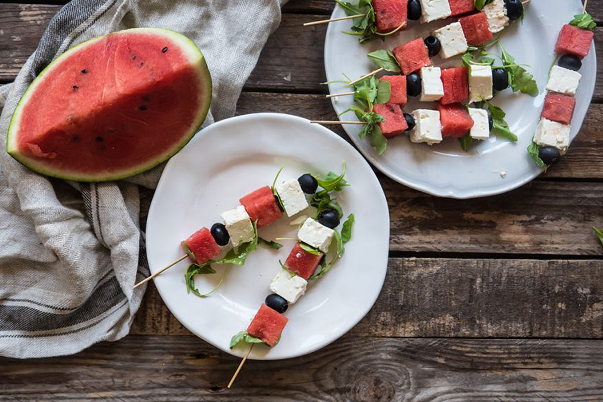 Spiedini: le migliori ricette di carne, di pesce o vegetariane 3 due piatti bianchi con sopra spiedini di anguria e feta, uno spicchio di cocomero accanto