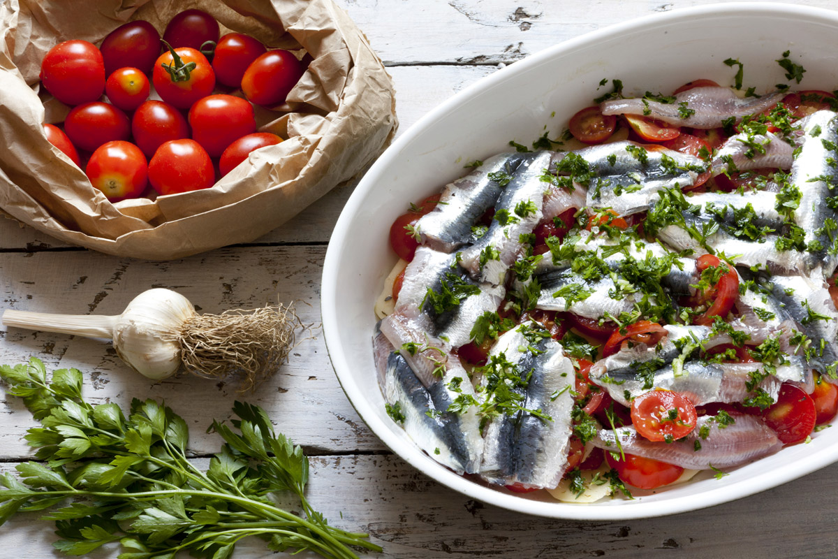 Ricette di pesce: antipasti, primi e secondi, tante idee veloci e gustose 45 teglia bianca ovale con tante alici alla pizzaiola, pacco di pomodorini accanto
