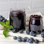 Marmellata di mirtilli senza zucchero: ricetta facile con Bimby e Fruttapec 2 In primo piano due vasetti di vetro con all'interno la marmellata di mirtilli neri e dei mirtilli sul vassoio