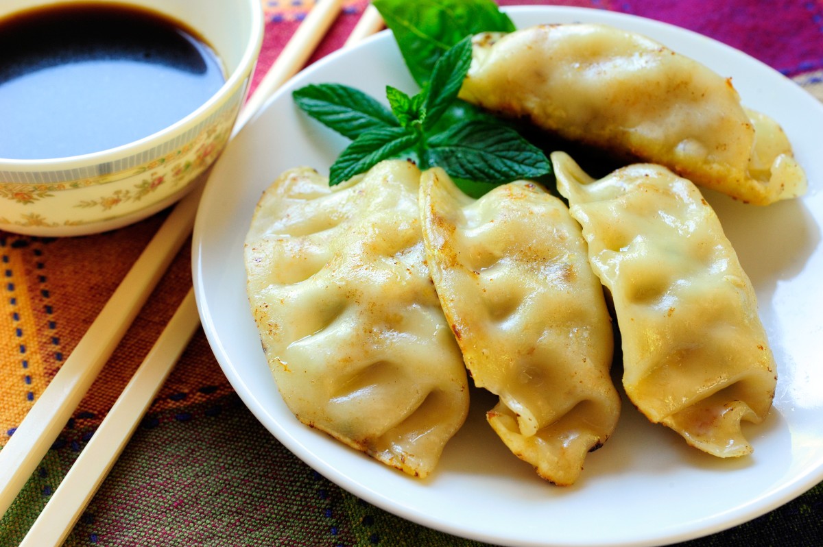 Ravioli: tante ricette semplici, gustose e innovative 1 piatto tondo con 4 ravioli cinesi e una ciotola con salsa di soia accanto