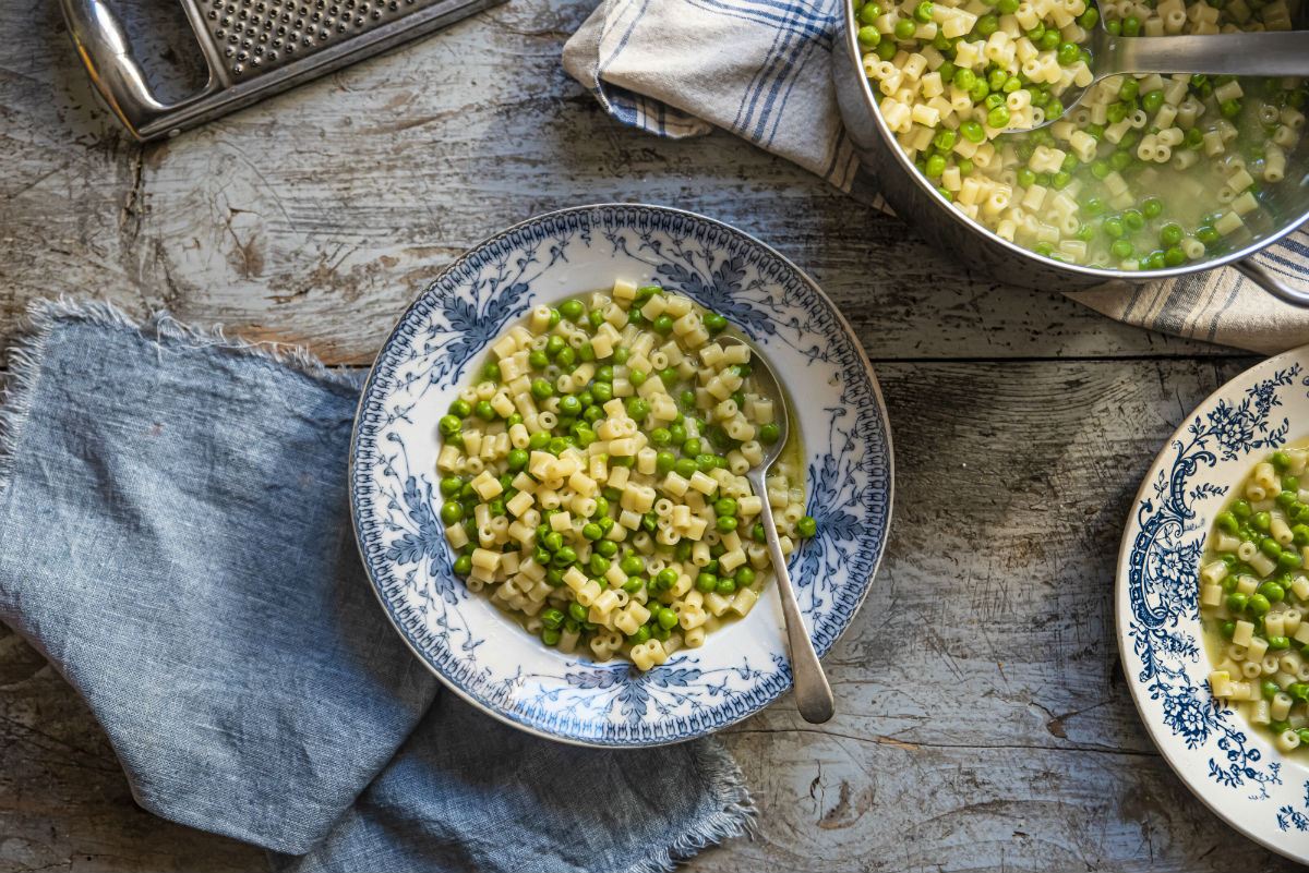Sughi per pasta fatti in casa: ricette veloci e sane piene di gusto 4 su tavolo di legno piatto con pasta e piselli sotto canovaccio blu e accanto ciottola piena di pasta e piselli