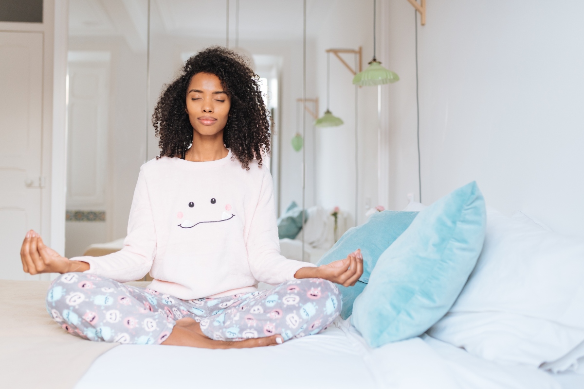 Meditazione: guida completa per iniziare e ottenere benefici reali 1 una giovane donna seduta sul letto in posizione loto per meditare