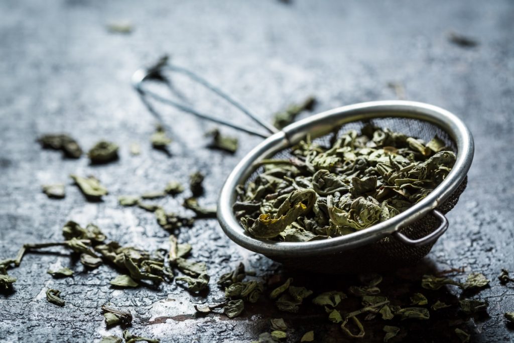 Tè verde: 3 benefici che non ti aspetti 1 benefici del tè verde: un colino con foglie di tè verde