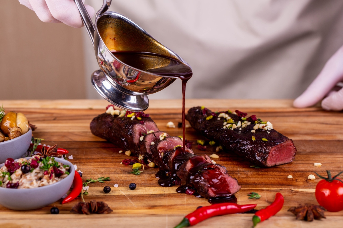 Ginepro: proprietà, benefici e usi in cucina 4 Una donna versa con una salsiera una salsa a base di ginepro su un piatto di carne rossa