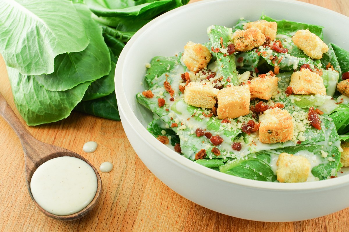 Caesar salad light: ricetta leggera e proteica 7 tavolo di legno con ciottola che contiene la caesar salad con crostini di pane e accanto la caesar salsa