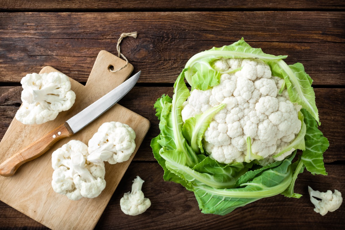 Cavolfiore: calorie e proprietà, come si cucina e migliori ricette 2 una testa di cavolfiore bianco e alcune cimette tagliate su un tagliere