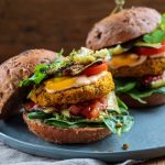 Hamburger vegetariano o veggie burger, la ricetta con lenticchie e patate 1 su tavolo di legno canovaccio sotto un piatto azzurro con un hamburger vegetariano fatto con patate e lenticchie