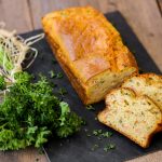 Plumcake salato: ricetta base e idee per farcirlo 1 su tavolo di legno, tagliere nero con plumcake salato al salmone e un mazzo di prezzemolo