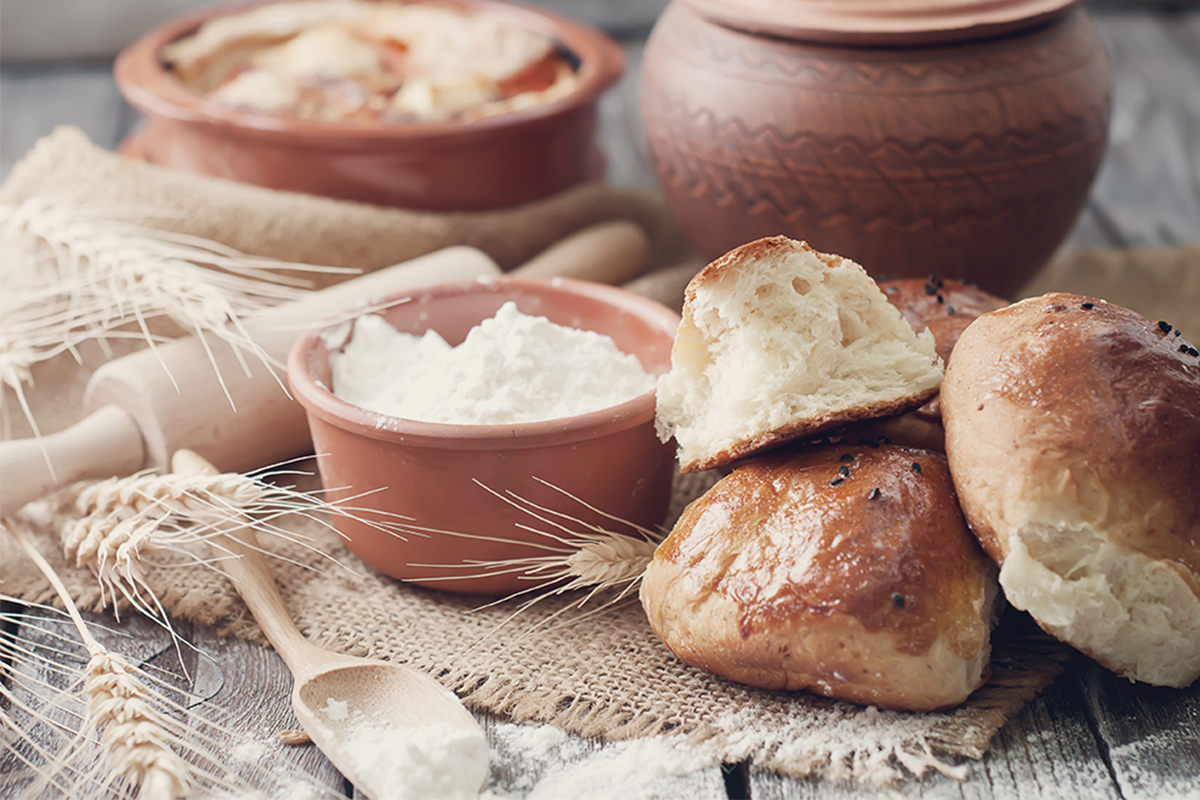 Pane fatto in casa: ricette genuine e semplici da provare 21 due pagnottine e un pezzo di pane bianco, una ciotola di farina e spighe di grano