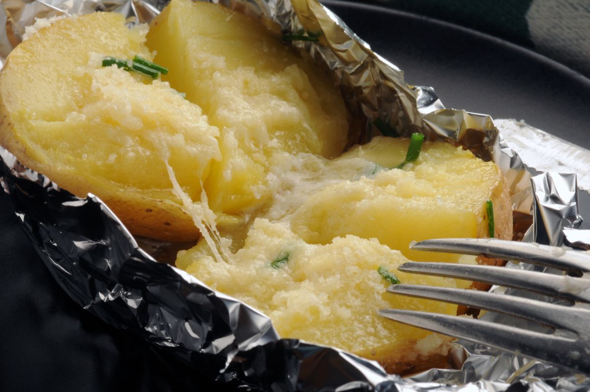 Patate al cartoccio: ricetta passo passo e video ricetta e come farle ripiene 2 primo piano delle patate al cartoccio calde in una carta di aluminio con una forchetta che sta per prendere le patate ripiene con formaggio