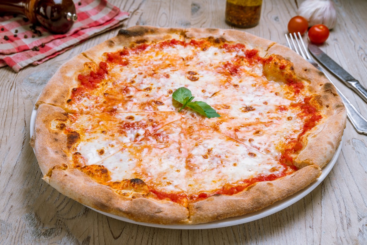 Pizza Margherita: la ricetta passo per passo da preparare in casa 5 su tavolo di legno piatto con la pizza margherita forchetta e coltello e pomodorini