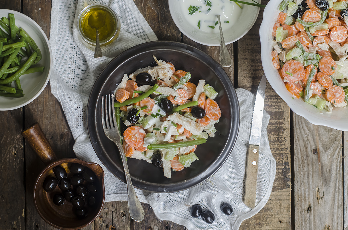Ricette con pollo: sane, leggere e ricche di sapore, tanti modi per cucinarlo 4 tavola a doghe di legno con sopra piatto nero con l'insalata di pollo, piatto di portata accanto