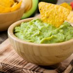 Guacamole: la ricetta della salsa messicana, calorie e varianti 1 vassoio di legno con sopra una ciotola di legno con guacamole e tacos