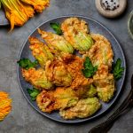 Fiori di zucca fritti senza pastella croccanti e leggeri 1 su tavolo da cucina di ardesia, piatto nero con fiori di zucca fritti e attorno fiori di zucca