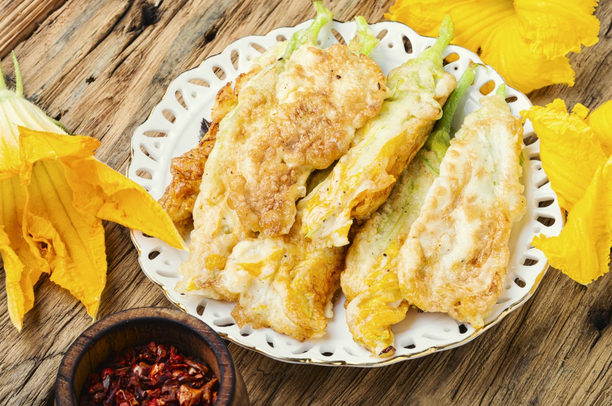 Fiori di zucca fritti senza pastella croccanti e leggeri 2 tavolo di legno con piatto bianco che contiene fiori di zucca fritti con attorno fiori di zucca