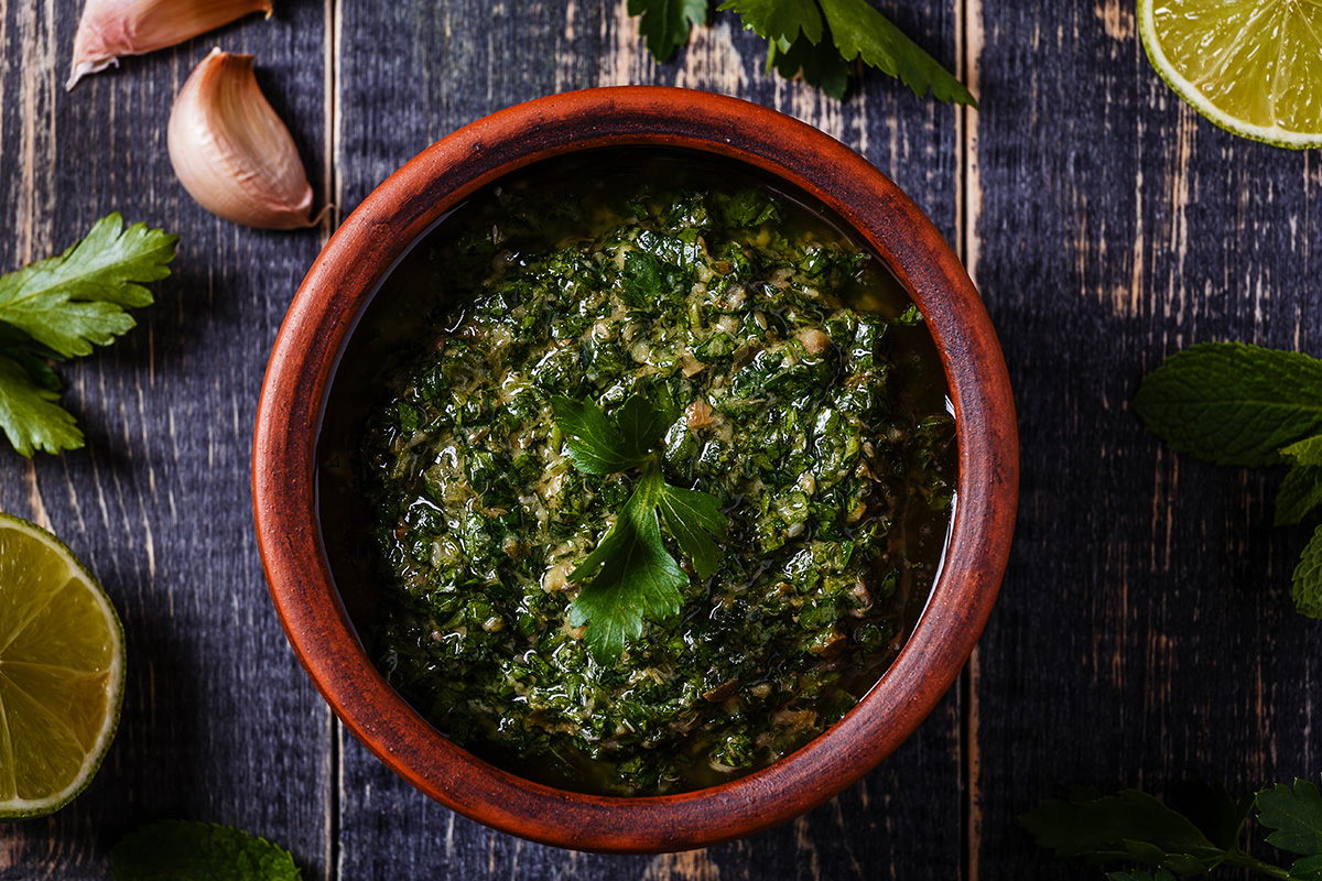 Salsa verde: ricetta facile di un classico piemontese 2 su tavolo da cucina, primo piano di una ciotola piena di salsa verde Piemontese con attorno alcuni ingredienti come limone, prezzemolo, aglio