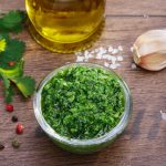 Salsa verde: ricetta facile di un classico piemontese 1 su tavolo di legno, ciotola di vetro con salsa verde alla Piemontese e attorno ingredienti come aglio, olio EVO, pepe e sale