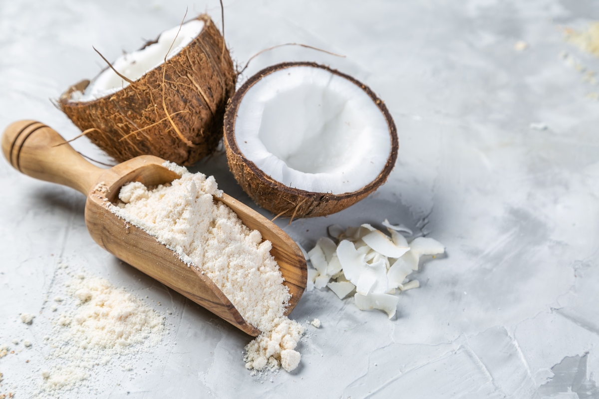 Cocco: dall'olio al latte, tutti i benefici del frutto tropicale 4 Una noce di cocco divisa in due e un cucchiaio di legno colmo di farina di cocco