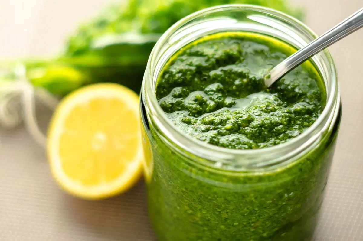 Pesto alla genovese: la ricetta originale per farlo in casa 3 primo piano di un vasetto di pesto alla Genovese con un cucchiaino e dietro mezzo limone e basilico