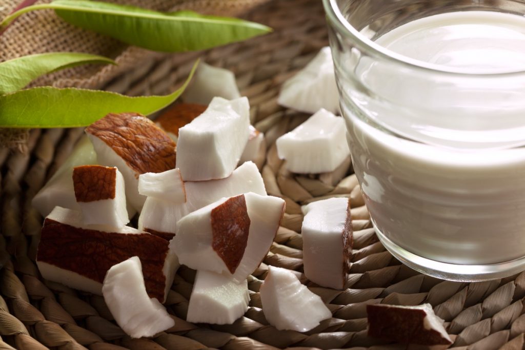 Latte di cocco: benefici, calorie, come farlo in casa e usi in cucina 4 un bicchiere colmo di latte di cocco e dei pezzetti di cocco accanto