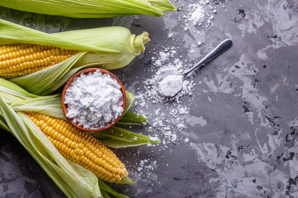 Maizena o amido di mais: cos’è, proprietà e usi in cucina 1 delle pannocchie di mais su un tavolo con accanto una ciotola piena di maizena