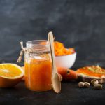 Marmellata di arance, la ricetta perfetta per una conserva golosa 3 un vasetto di vetro pieno di marmellata di arance, anche spalmata su una fetta di pane, e metà arancia accanto