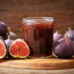 Marmellata di fichi senza zucchero 2 in primo piano su un tavolo di legno, un barattolo di vetro con la marmellata di fichi e dei fichi tagliati a metà intorno.