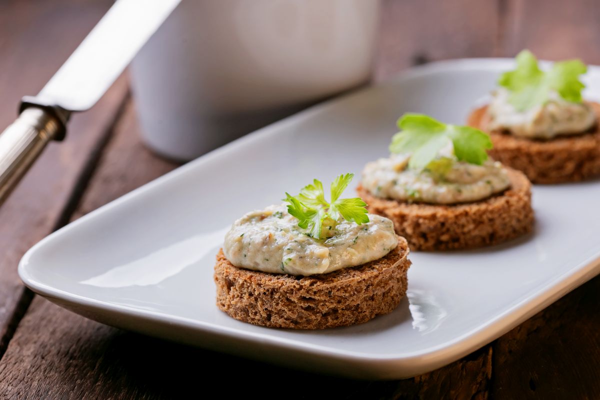 Salsa tonnata: la ricetta sana fatta in casa 4 u tavolo di legno, piatto rettangolare con crostini con salsa tonnata e erbe aromatiche