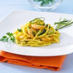 Trofie zucchine e gamberetti: la ricetta facile 1 su tavolo di marmo, piatto bianco con un tovagliolo arancione, nel piatto trofie con zucchine e gamberetti