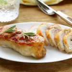 Involtini di tacchino ripieni di verdure: la ricetta in padella o al forno 2 in primo piano su un piatto piano bianco, gli involtini di tacchino tagliati a fette e decorati con un rametto di rosmarino su una tavola di legno apparecchiata