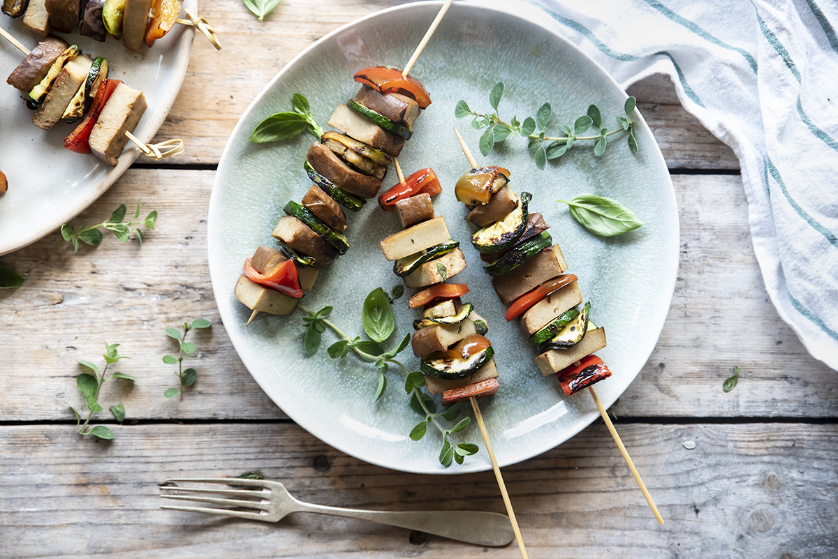 Ricette con seitan: come cucinarlo e ricette gustose 1 su base di legn piatto chiaro con 3 spiedini con seitan e verdure